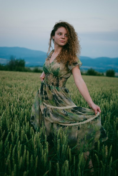 白天，一位身穿绿色和棕色花朵连衣裙的妇女站在绿色的草地上